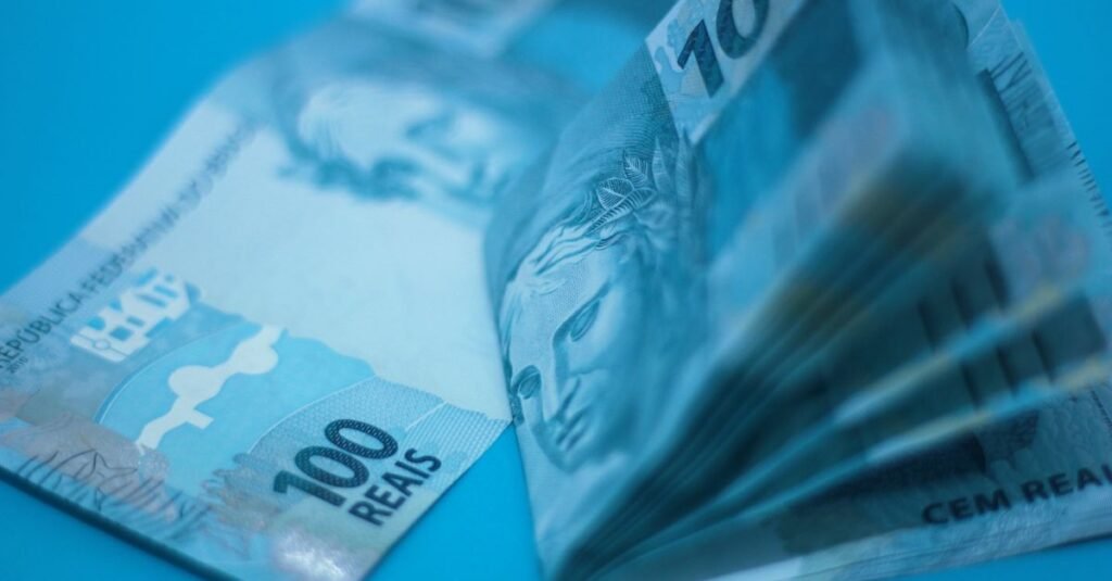 Stack of 100 Brazilian real notes placed on a blue surface, showcasing currency details.