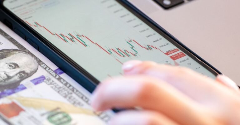 Close-up of a smartphone displaying stock market data over a dollar bill on a desk.